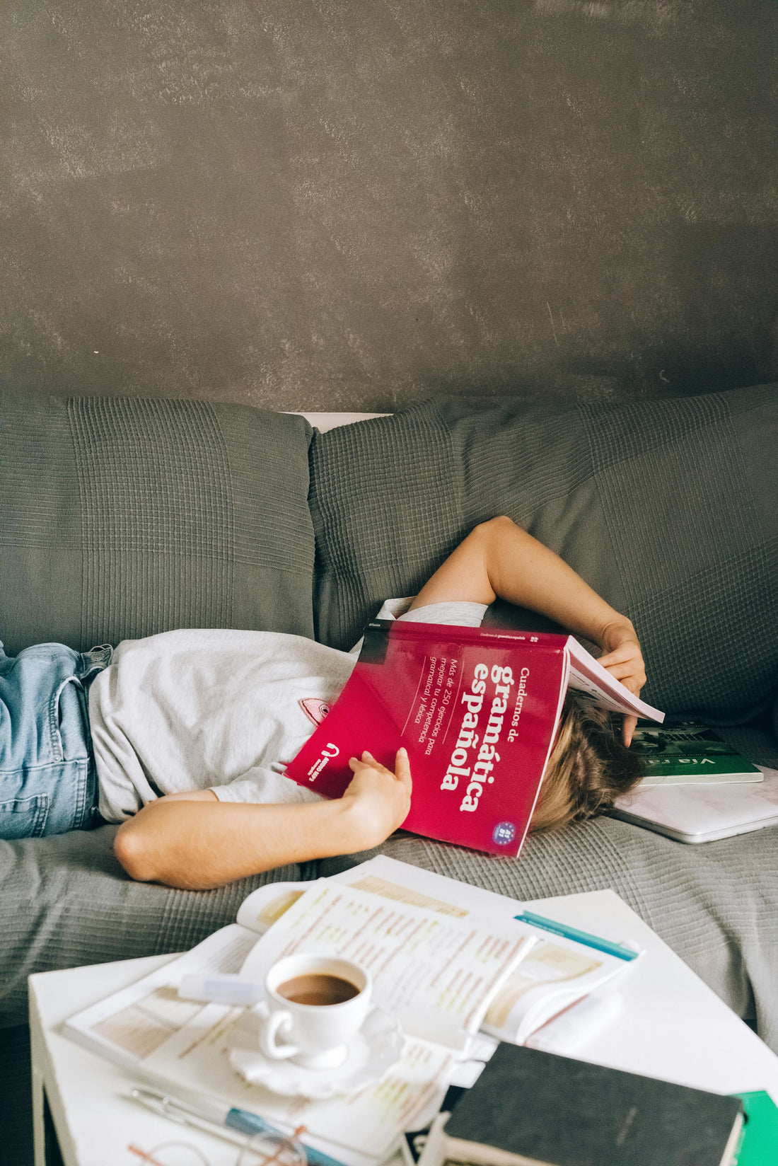 Woman lying on the couch with books on her face and books and coffee on the table.