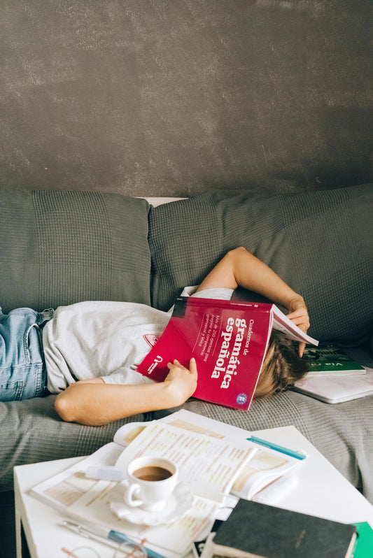 Woman lying on the couch with books on her face and books and coffee on the table.